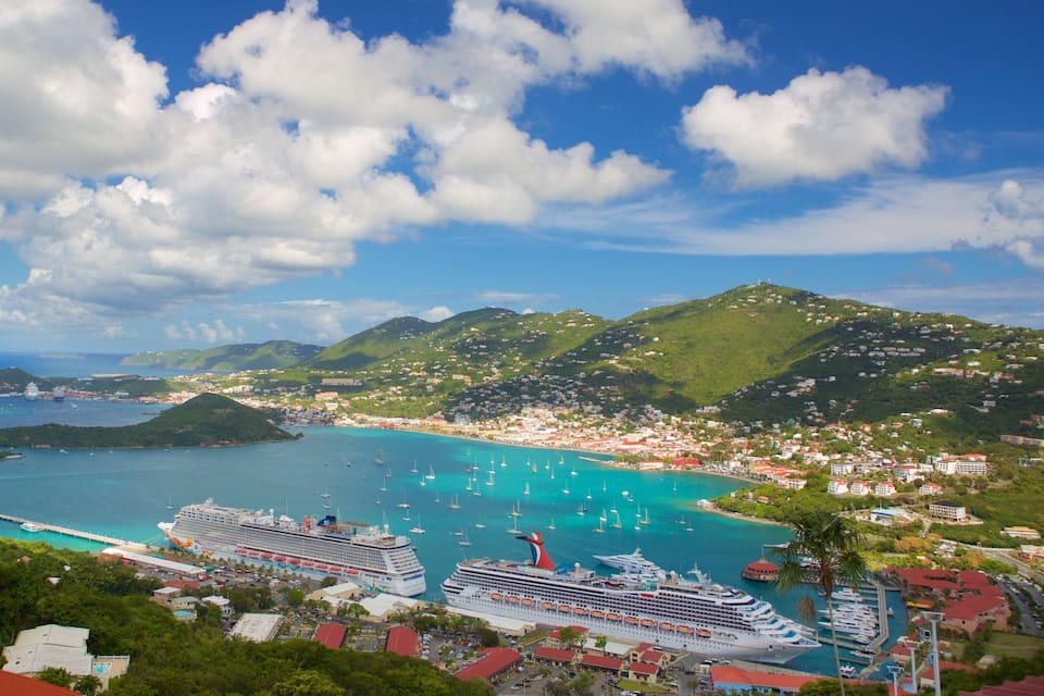 A coastal town with a cruise ship docked, clear turquoise waters, and green hills in the background.