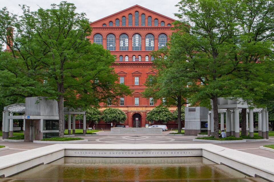 A red brick building with arched windows, surrounded by trees and a reflecting pool.