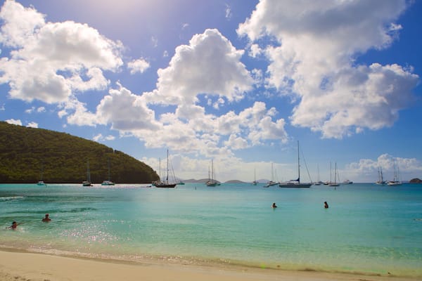 A turquoise sea with boats and people swimming.