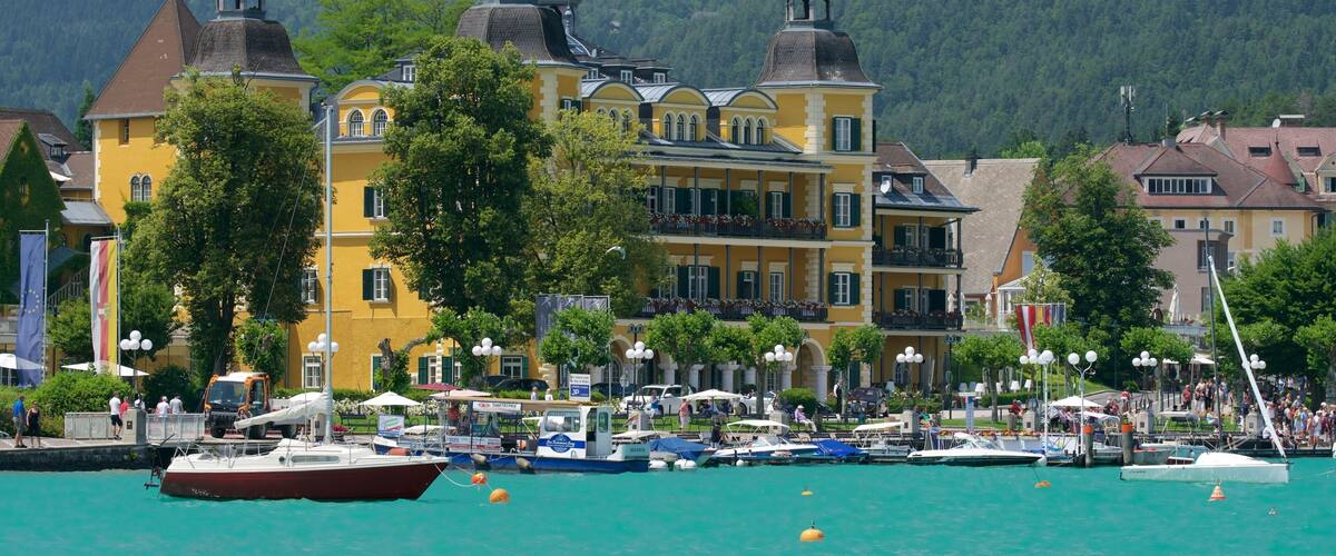 A waterfront town with colorful buildings, a marina, and a forested mountain backdrop.
