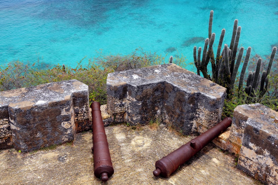 Rusted cannons on a weathered stone platform by turquoise waters.