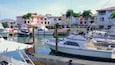Un port de plaisance où sont amarrés plusieurs bateaux, entouré d’immeubles à étages dotés de balcons et de palmiers.