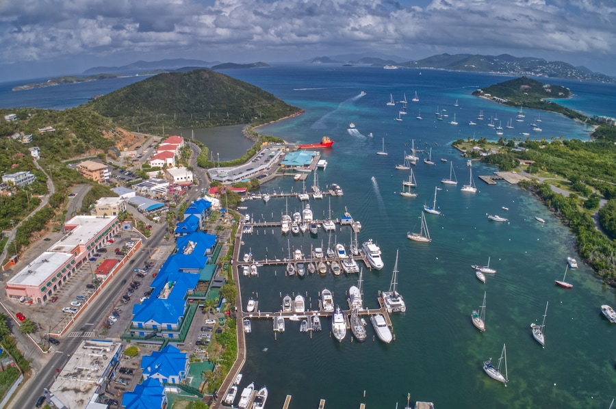 Un puerto deportivo con numerosos veleros amarrados, rodeado de exuberante vegetación y montañas al fondo.