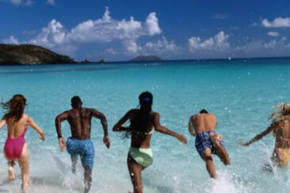 A group of people running into the sea on a beach with clear blue water and a clear sky.