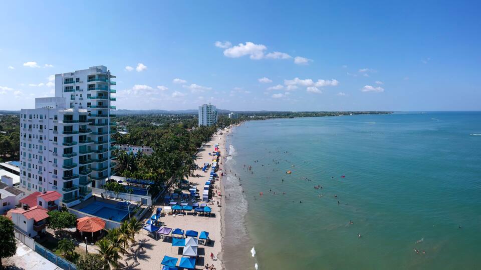 A coastal cityscape with a beach, palm trees, and high-rise buildings.