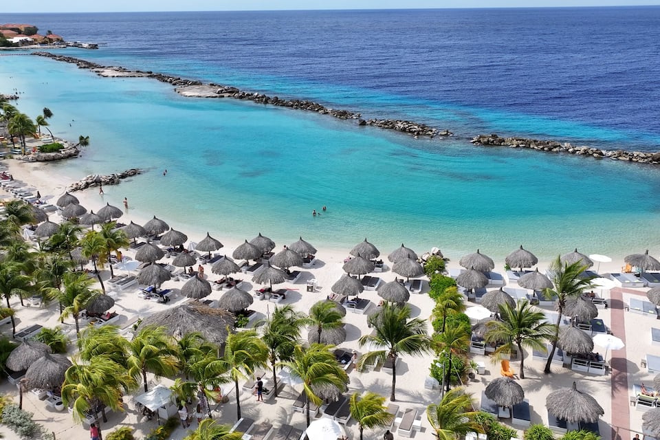 Une plage tropicale aux eaux turquoise et limpides, agrémentée de parasols en feuilles de palmier et de palmiers.