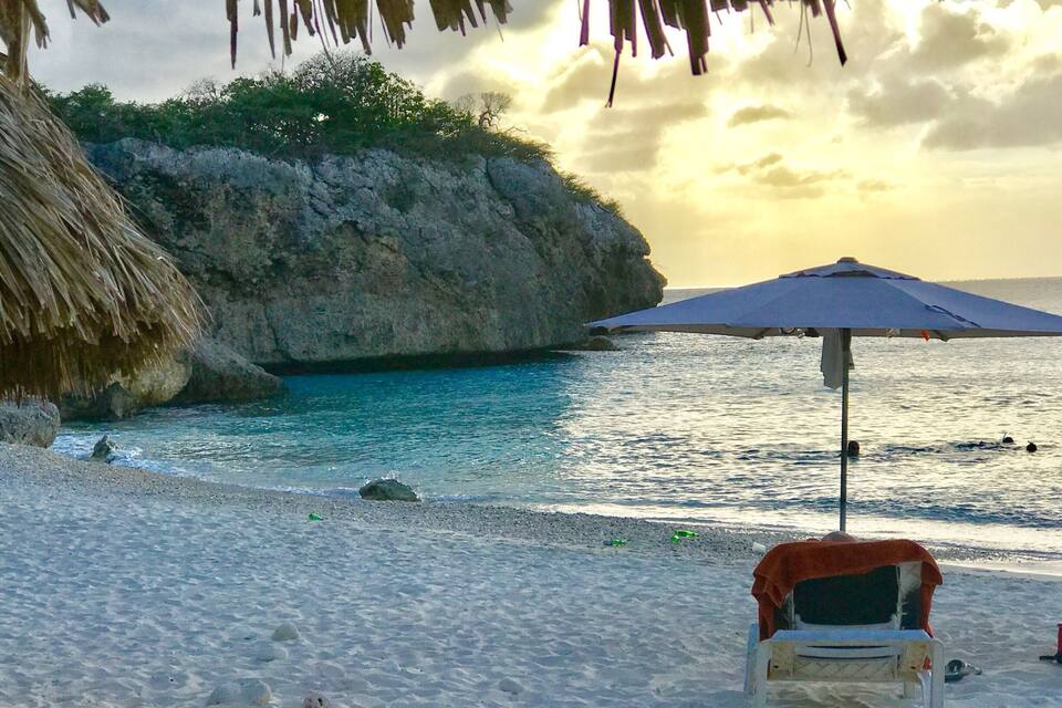 Een strand met een rieten dak, een stoel en een parasol.