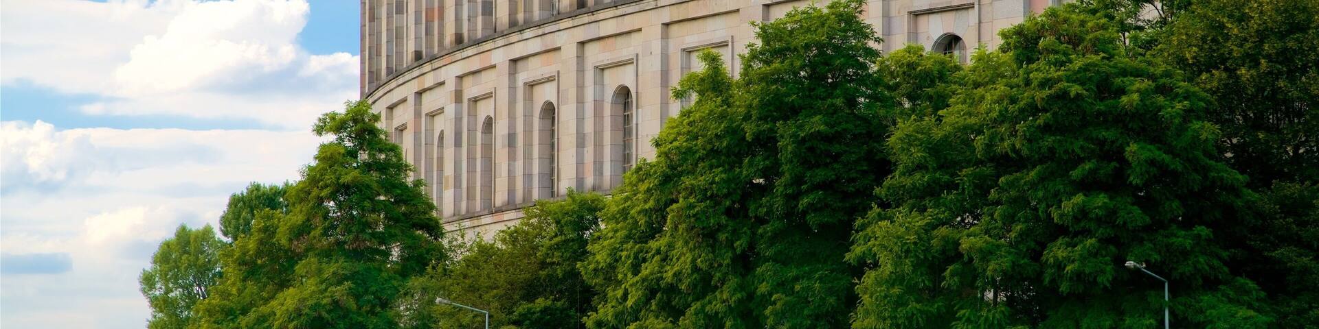 A large, historic building with arched windows and a curved facade, surrounded by lush green trees.