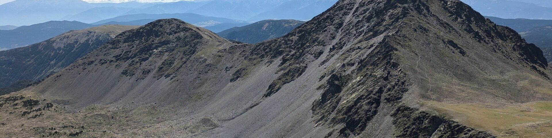 A rugged mountain landscape with rocky outcrops and distant snow-capped peaks under a clear sky.