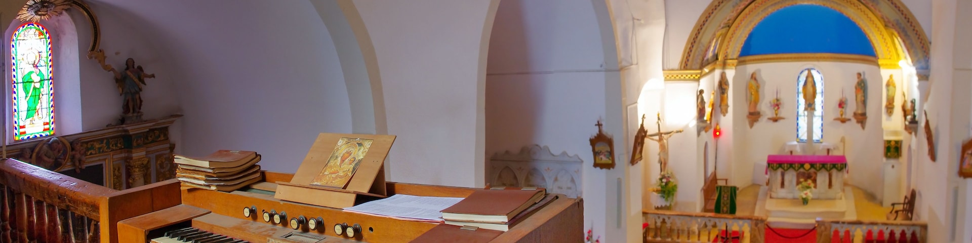 An organ with sheet music, a stained glass window, and a church interior with arched ceilings and religious statues.