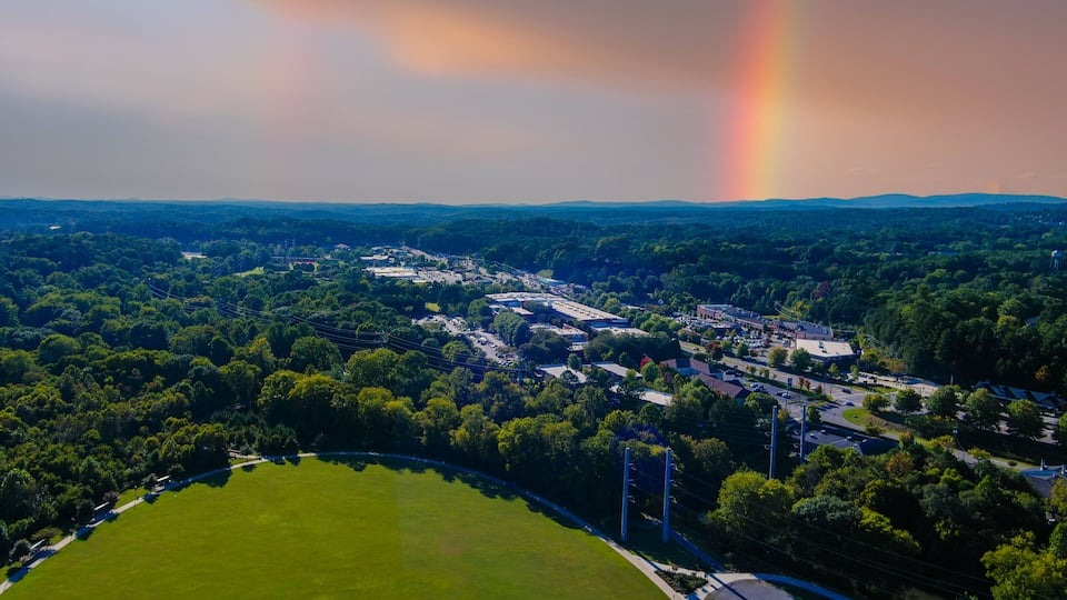 an aerial shot of the vast miles of lush green trees and grass with buildings nestled among the trees and powerful clouds and a rainbow at Etowah River Park in Canton Georgia USA