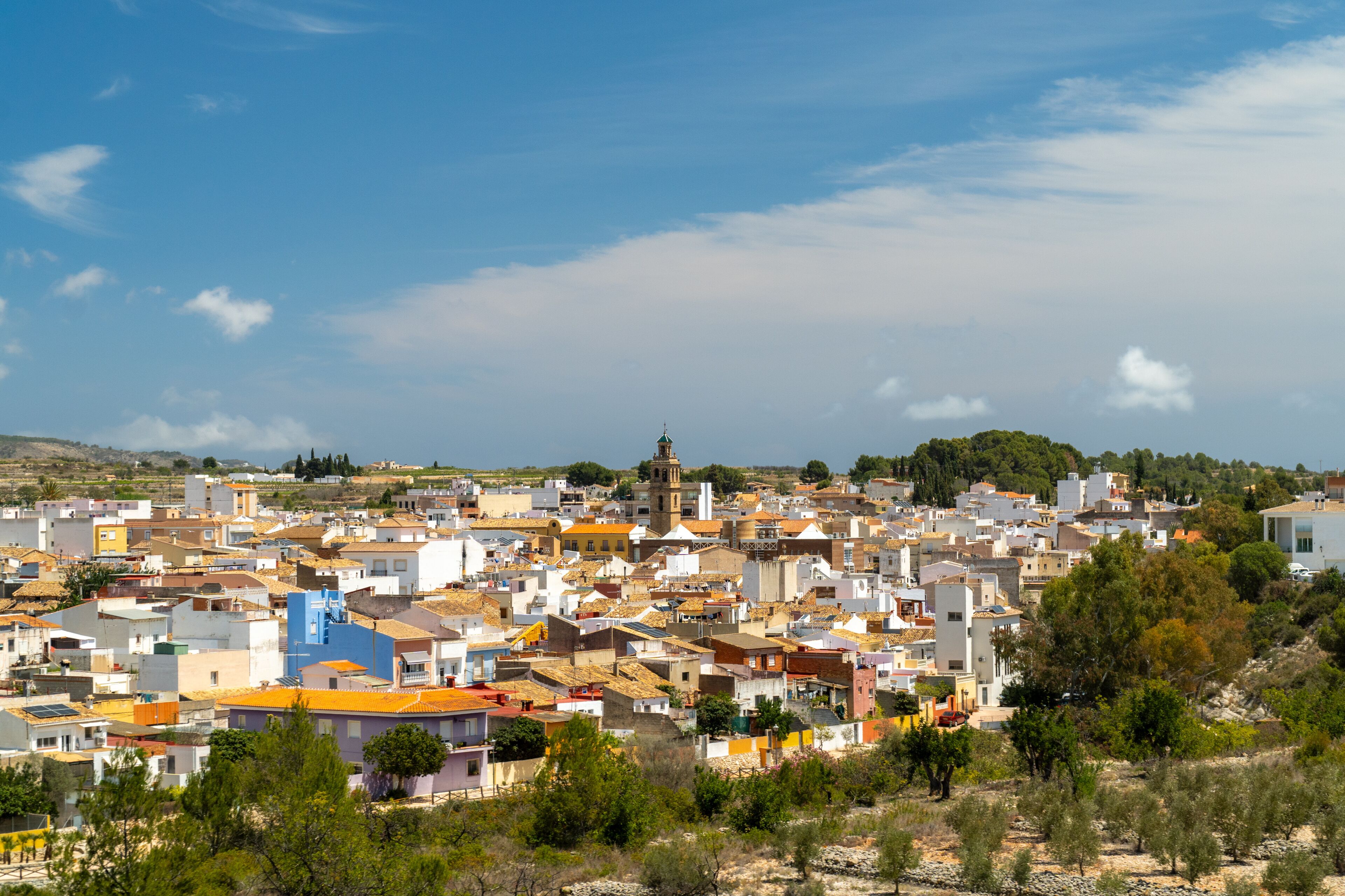 A coastal town with a mix of modern and traditional buildings, a prominent bell tower, and a clear blue sky.