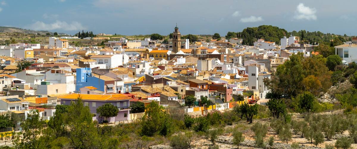 A coastal town with a mix of modern and traditional buildings, a prominent bell tower, and a clear blue sky.