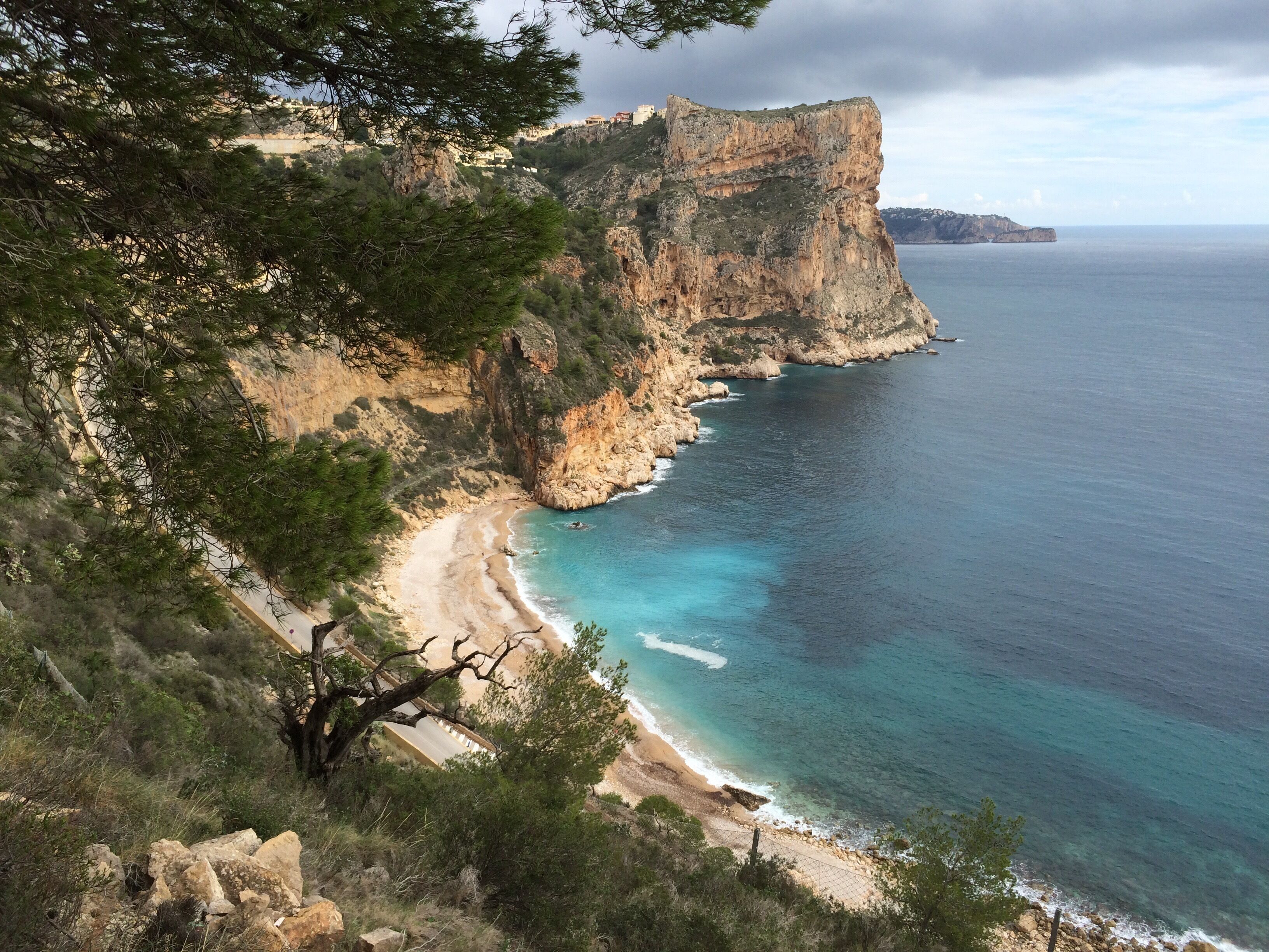A coastal landscape with a rocky cliff, a sandy beach, and clear blue waters.