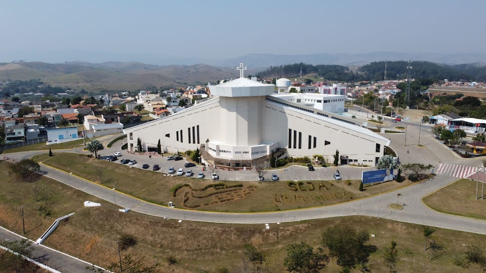 A large white church with a cross on top, surrounded by a parking lot and a road.