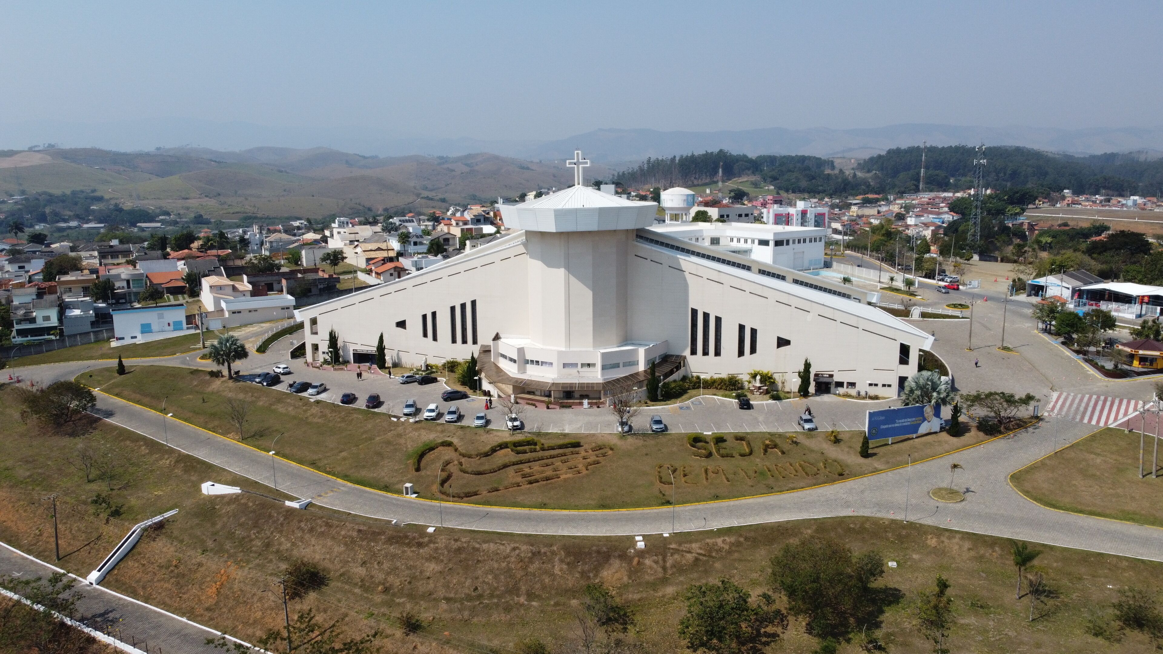 A large white church with a cross on top, surrounded by a parking lot and a road.