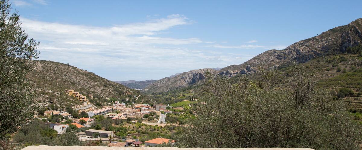 A valley with a small town nestled between hills, olive trees, and rocky terrain.
