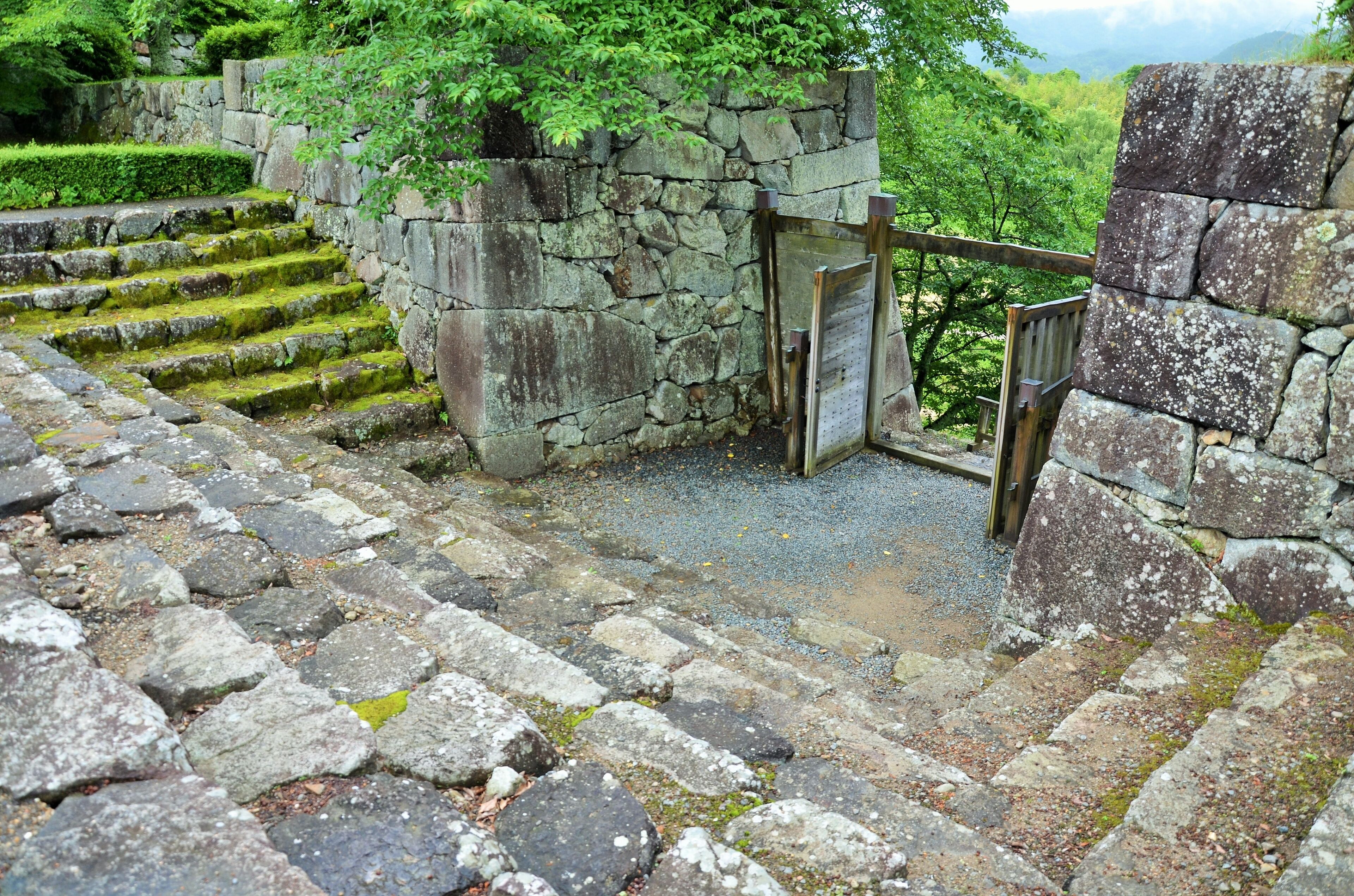 Stone steps leading up to a gate, surrounded by greenery and stone walls.