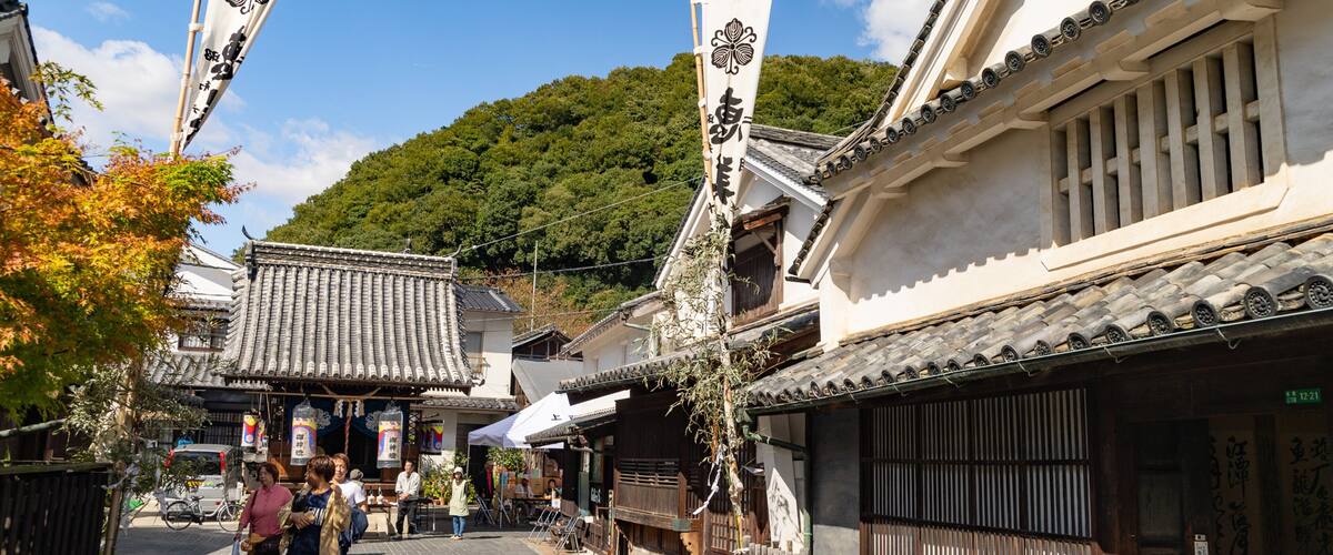 A traditional Japanese street with wooden buildings, tiled roofs, and a bamboo fence.