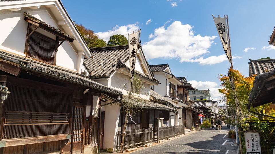 A traditional Japanese street with wooden buildings, tiled roofs, and a clear blue sky.