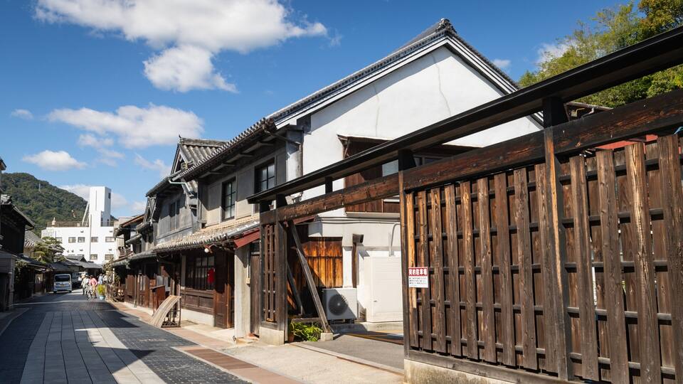 A traditional Japanese street with wooden fences, buildings with tiled roofs, and a clear blue sky.