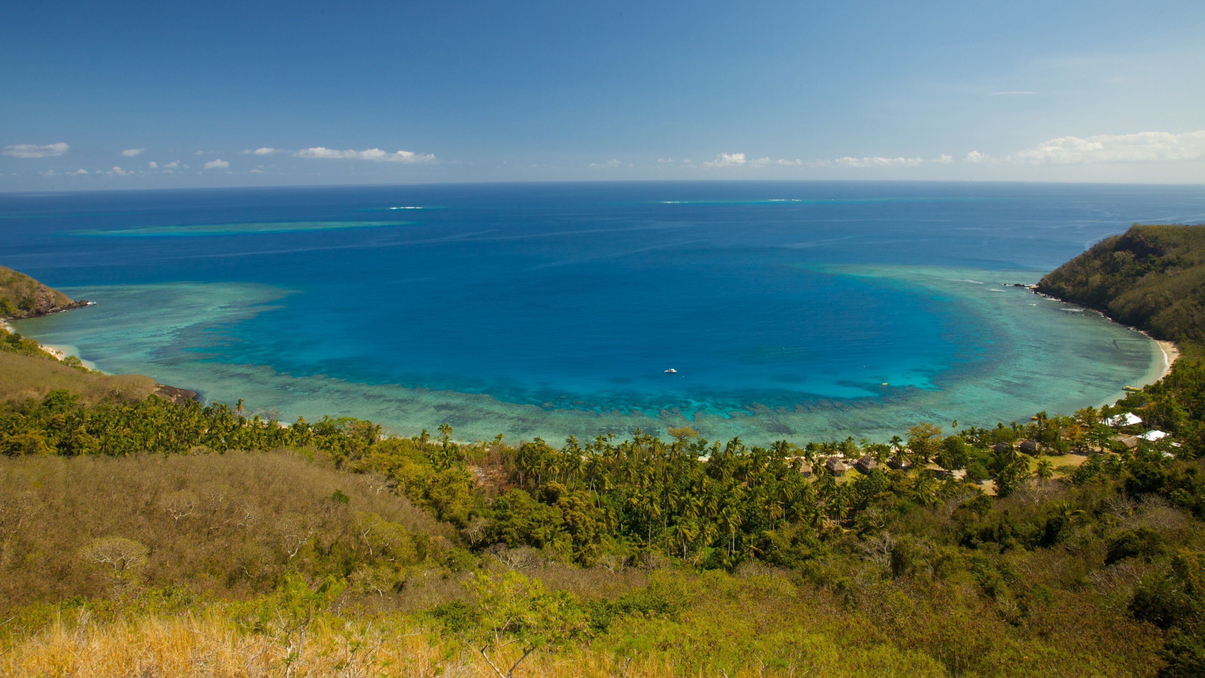 A tropical coastal landscape with clear blue waters, a sandy beach, and lush greenery.
