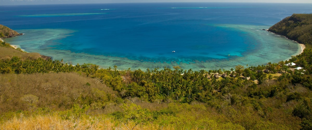 A tropical coastal landscape with clear blue waters, a sandy beach, and lush greenery.
