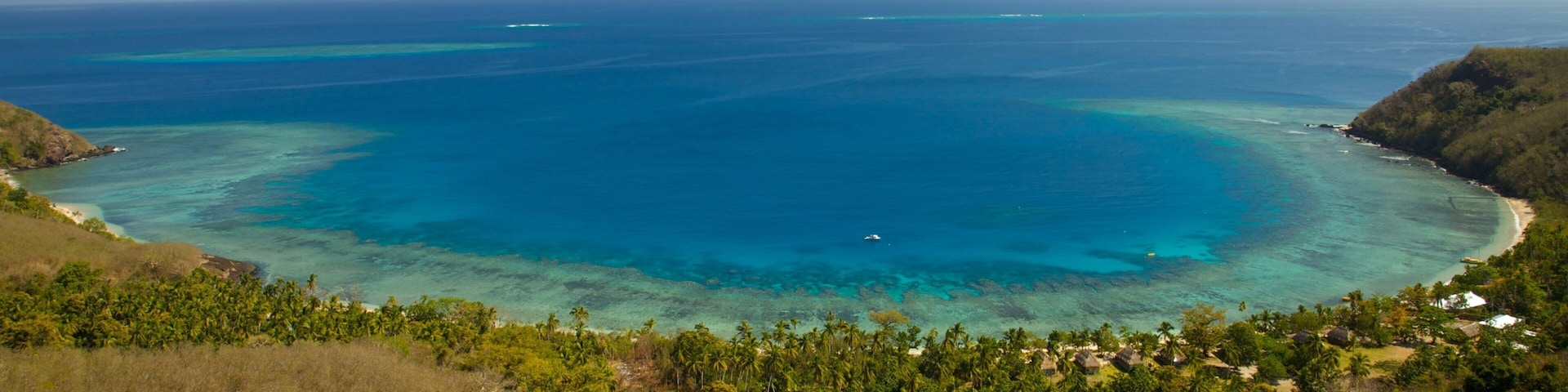 A tropical coastal landscape with clear blue waters, a sandy beach, and lush greenery.