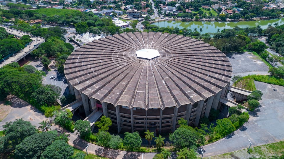 An aerial view of a circular building surrounded by greenery and a body of water.