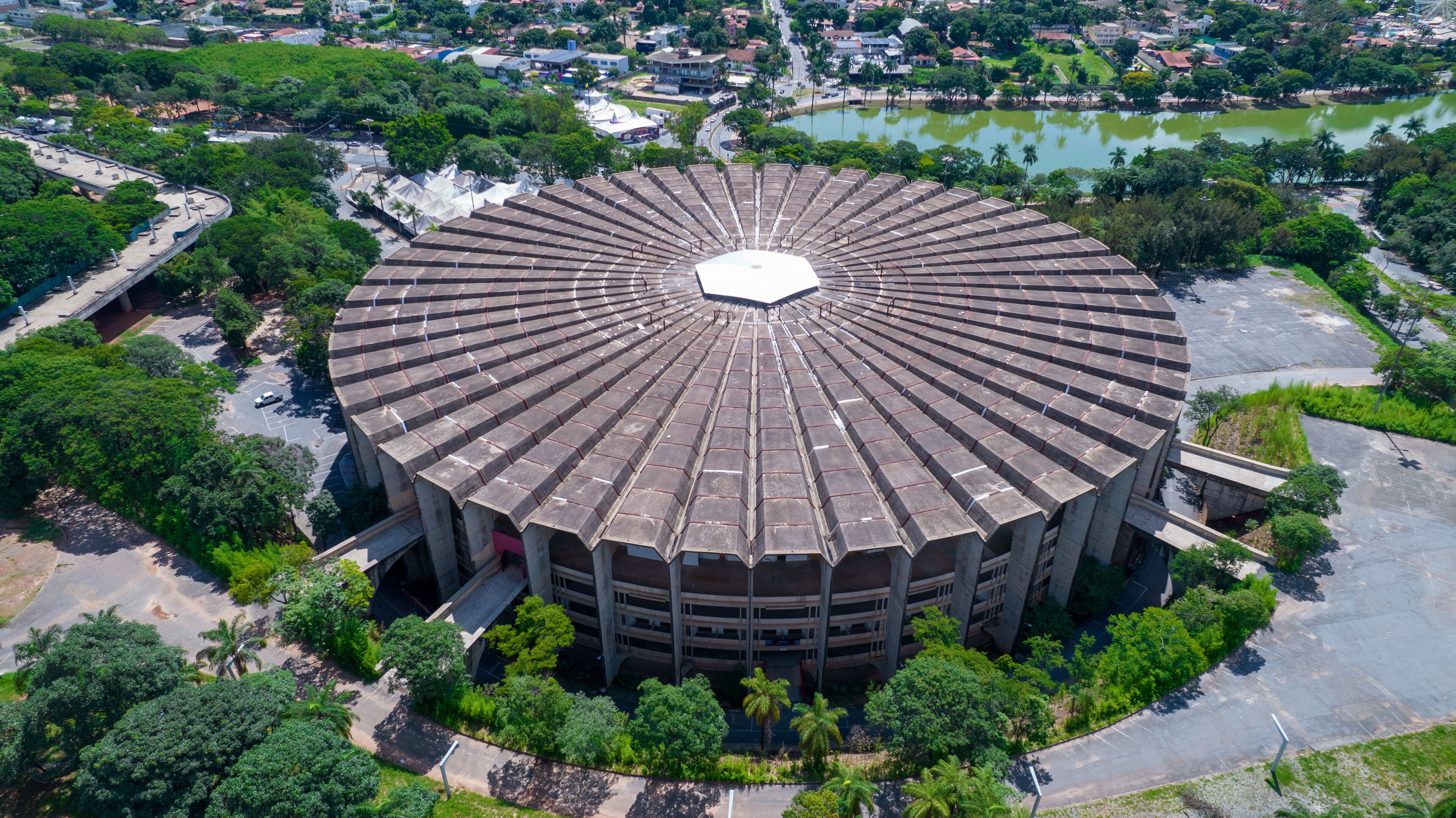An aerial view of a circular building surrounded by greenery and a body of water.