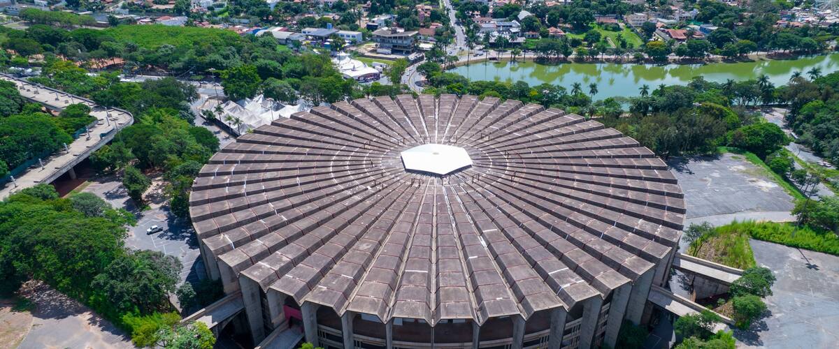An aerial view of a circular building surrounded by greenery and a body of water.
