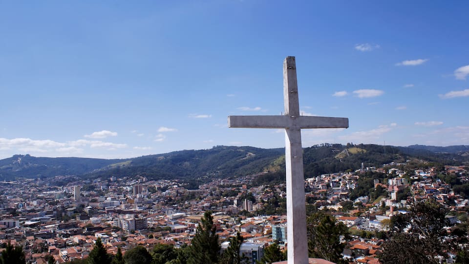 A cross monument overlooking a cityscape with hills in the background.