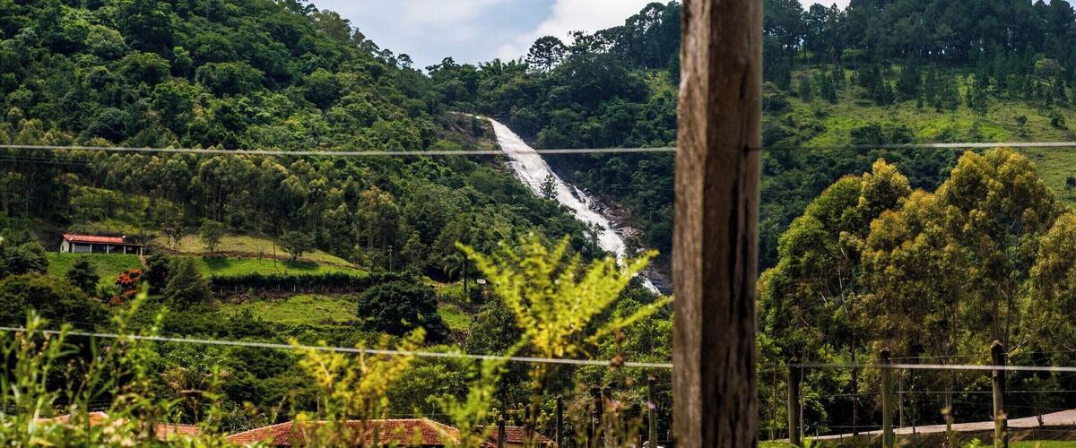 A lush green landscape with a waterfall cascading down a hillside, surrounded by dense vegetation and a few buildings in the foreground.