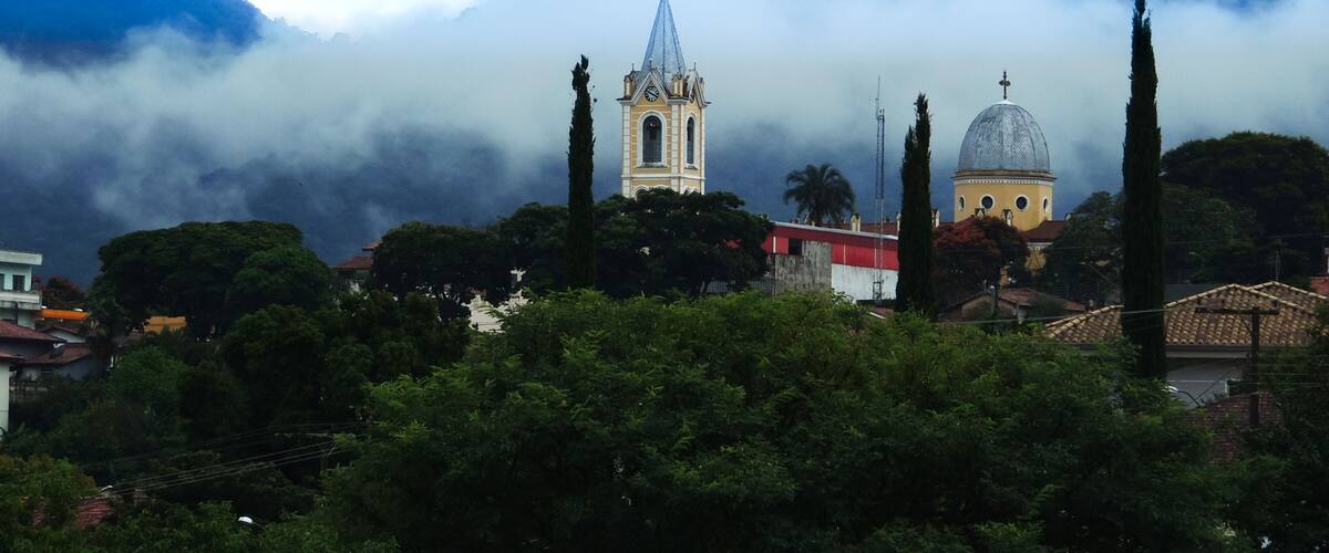 Large image of a beautiful misty mountain landscape in a small town called Joanopolis in the countryside of Brazil. Catholic church clock and bell tower view among foggy mountains and stunning nature