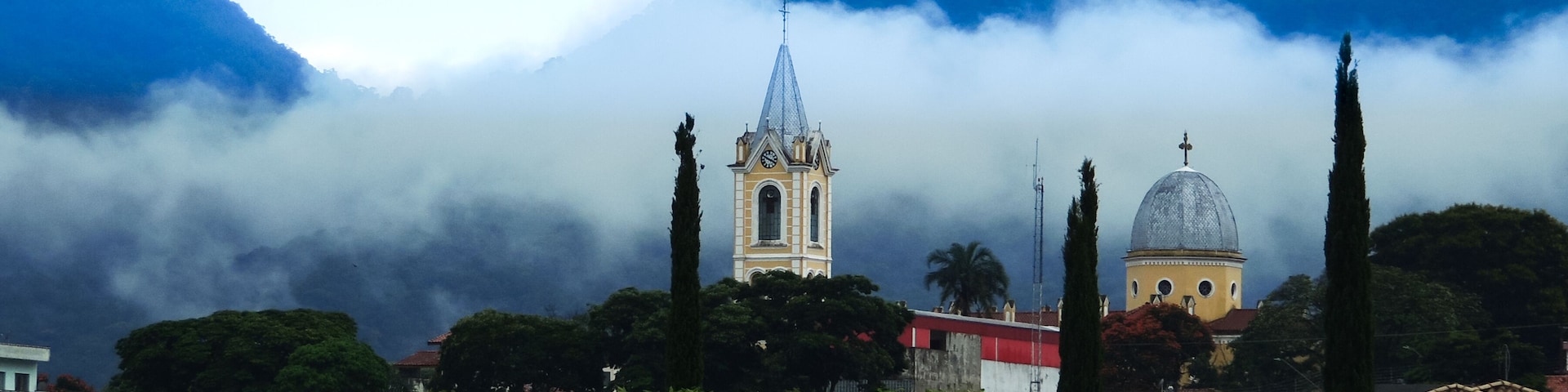 Large image of a beautiful misty mountain landscape in a small town called Joanopolis in the countryside of Brazil. Catholic church clock and bell tower view among foggy mountains and stunning nature
