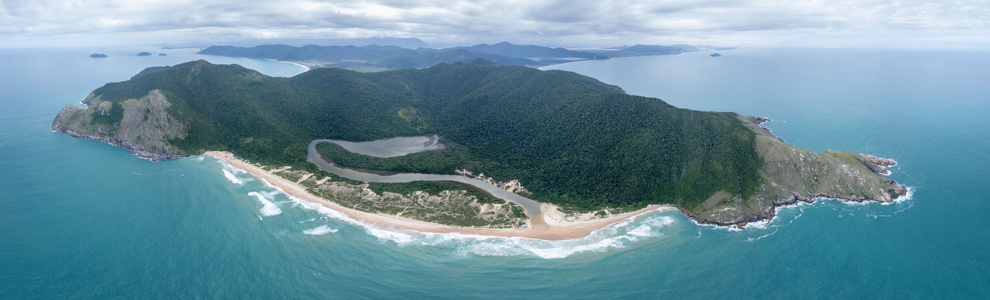 An aerial view of a tropical island with a winding road, a beach, and surrounding ocean.