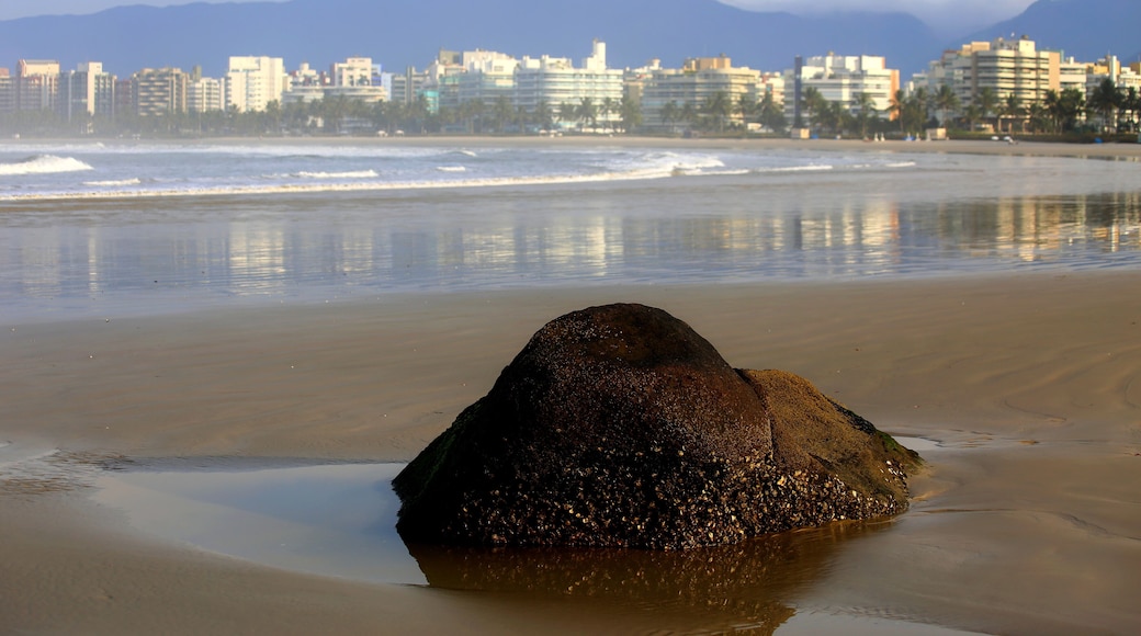 A beach with sand and calm waters, a stone in the foreground and a city in the horizon. Riviera de Sao Lourenco, Bertioga, Brazil