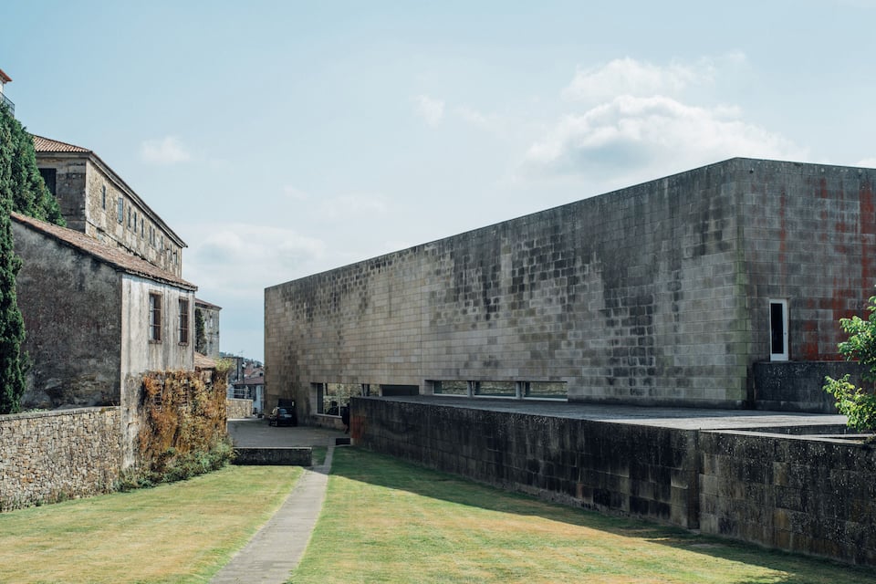 A courtyard with a stone wall, a grassy area, and a building with a tiled roof.