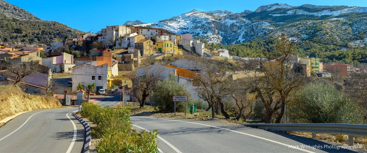 A winding road through a hilly village with colorful buildings and a snow-capped mountain in the background.