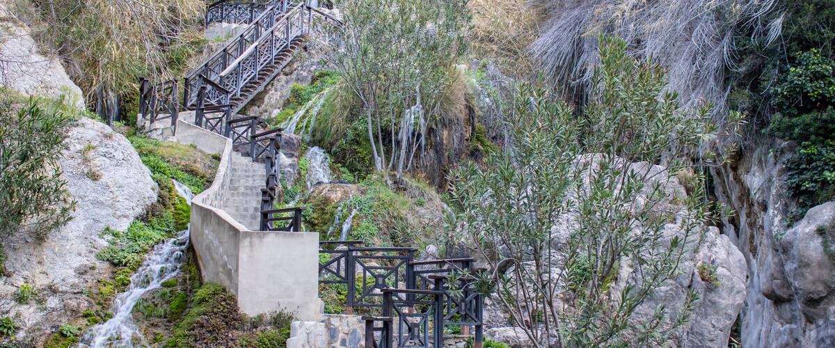 A stone staircase leading up a rocky hillside with a small waterfall at the bottom.