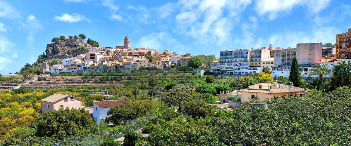 A coastal town with buildings on a hillside, a prominent tower, and lush greenery.