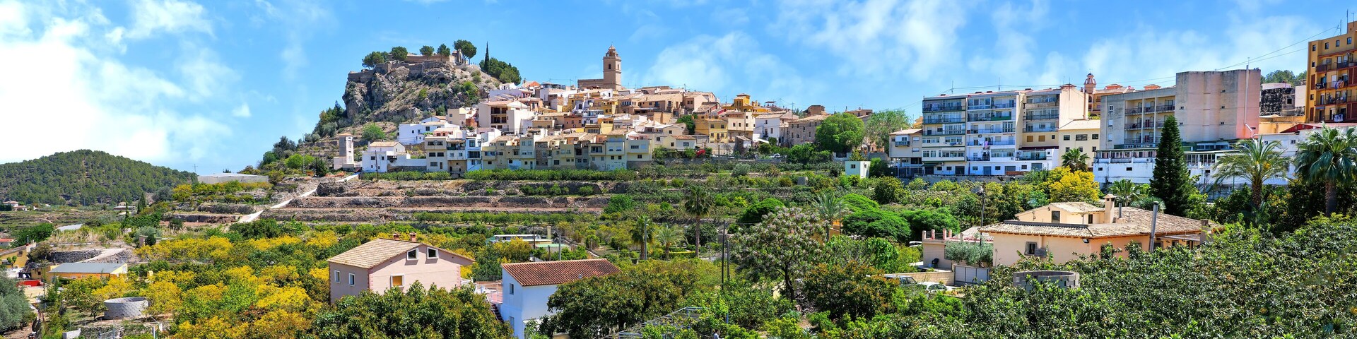 A coastal town with buildings on a hillside, a prominent tower, and lush greenery.