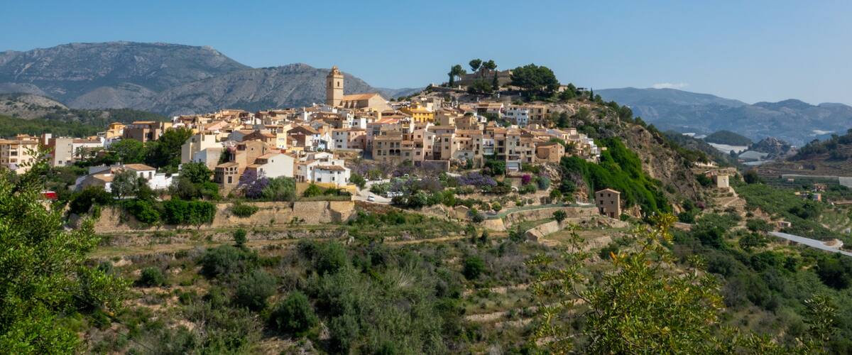 A coastal town with terraced buildings, a prominent tower, and mountains in the background.