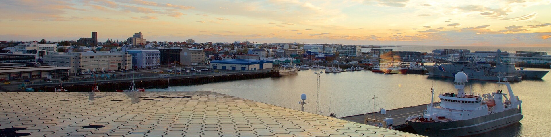 Un puerto con barcos, el perfil de una ciudad y un atardecer.