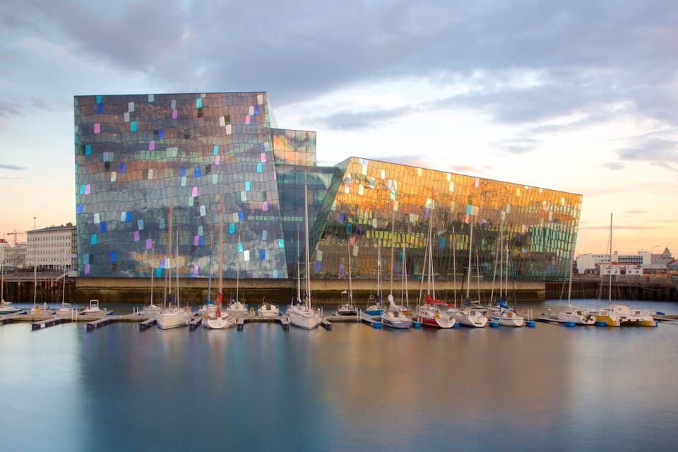 Un edificio moderno con facciata in vetro riflettente, circondato da una marina con diverse imbarcazioni.