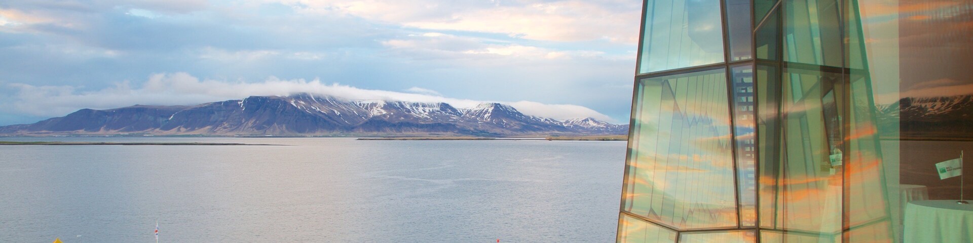 Un edificio moderno de vidrio con vistas a un lago tranquilo y montañas nevadas a lo lejos.