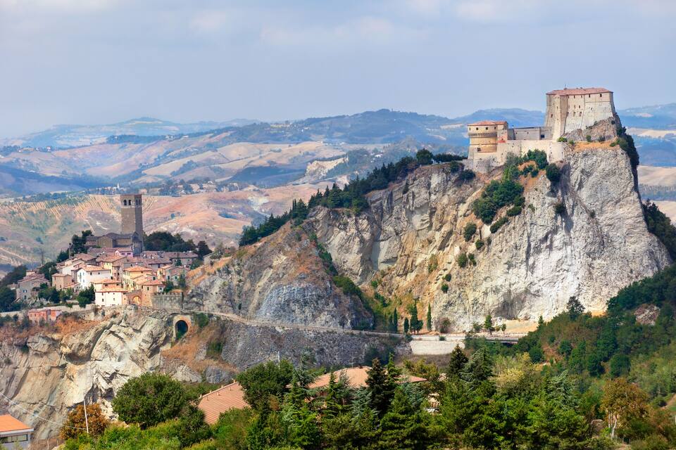 A historic town perched on a cliff with a prominent tower and a fortified structure on top.