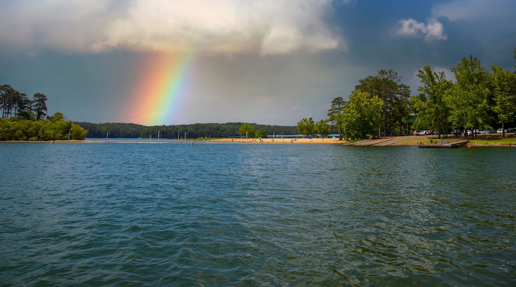 a gorgeous rainbow over Lake Allatoona with a beach and rippling blue lake water surrounded by lush green trees, grass and plants with clouds at Victoria Beach in Acworth Georgia USA