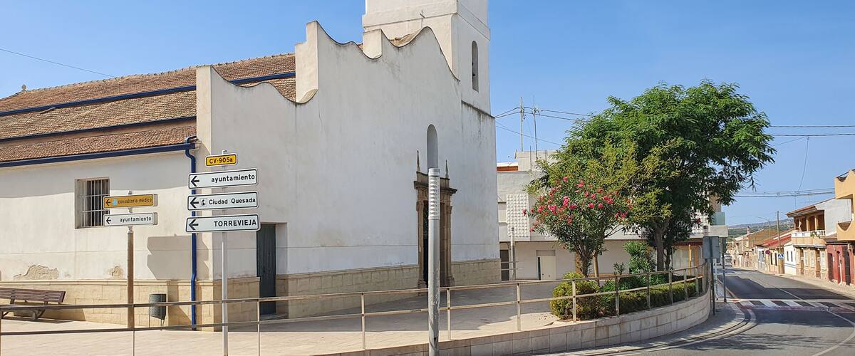 A white church with a clock tower, surrounded by a street with signs pointing to various locations.