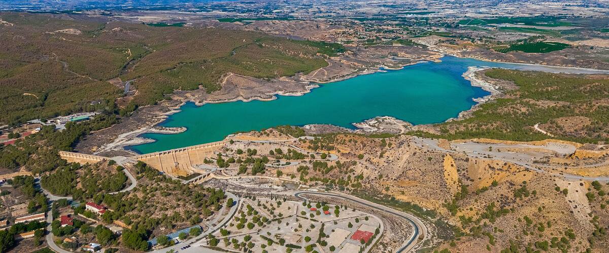 An aerial view of a coastal area with a large body of water, a dam, and surrounding hills.